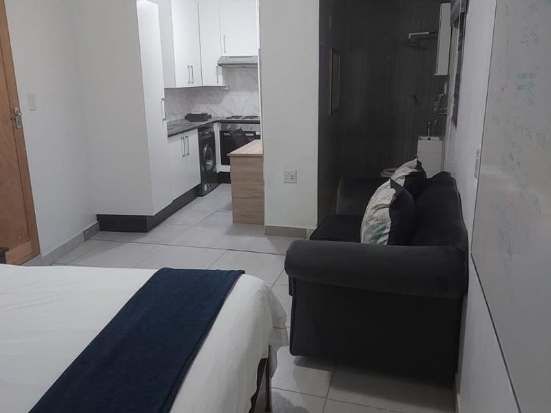 Open-plan studio layout featuring a compact kitchen with built-in cabinetry, tiled flooring, and an adjacent bathroom area.