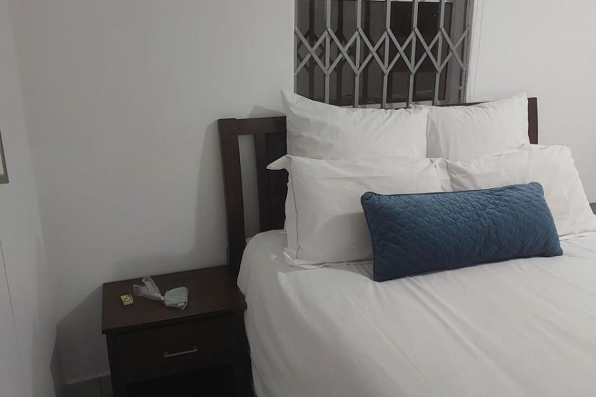 A simple bedroom featuring tiled flooring, a window fitted with a security gate, and a roller blind.