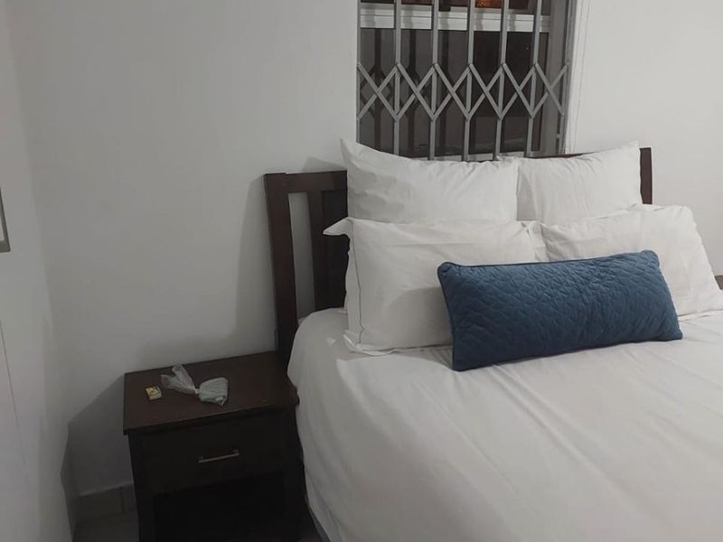 A simple bedroom featuring tiled flooring, a window fitted with a security gate, and a roller blind.