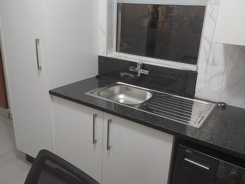 A functional laundry area featuring modern white cabinetry, a dark granite countertop, and a stainless steel sink with a window view.