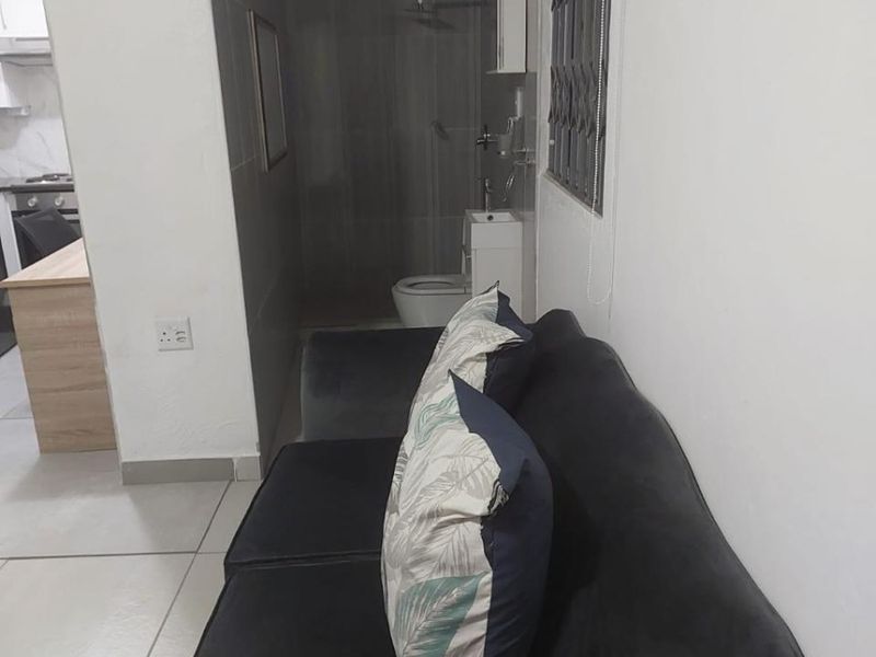 Open plan living area featuring tiled floors and a compact bathroom with a shower, toilet, and vanity basin.