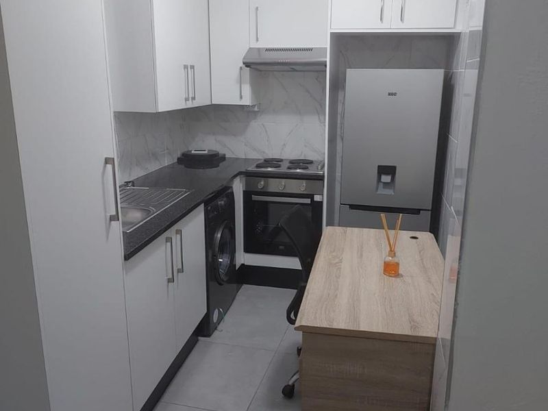 Compact modern kitchen featuring white cabinetry, dark countertops, built-in oven with extractor fan, and tiled finishes.