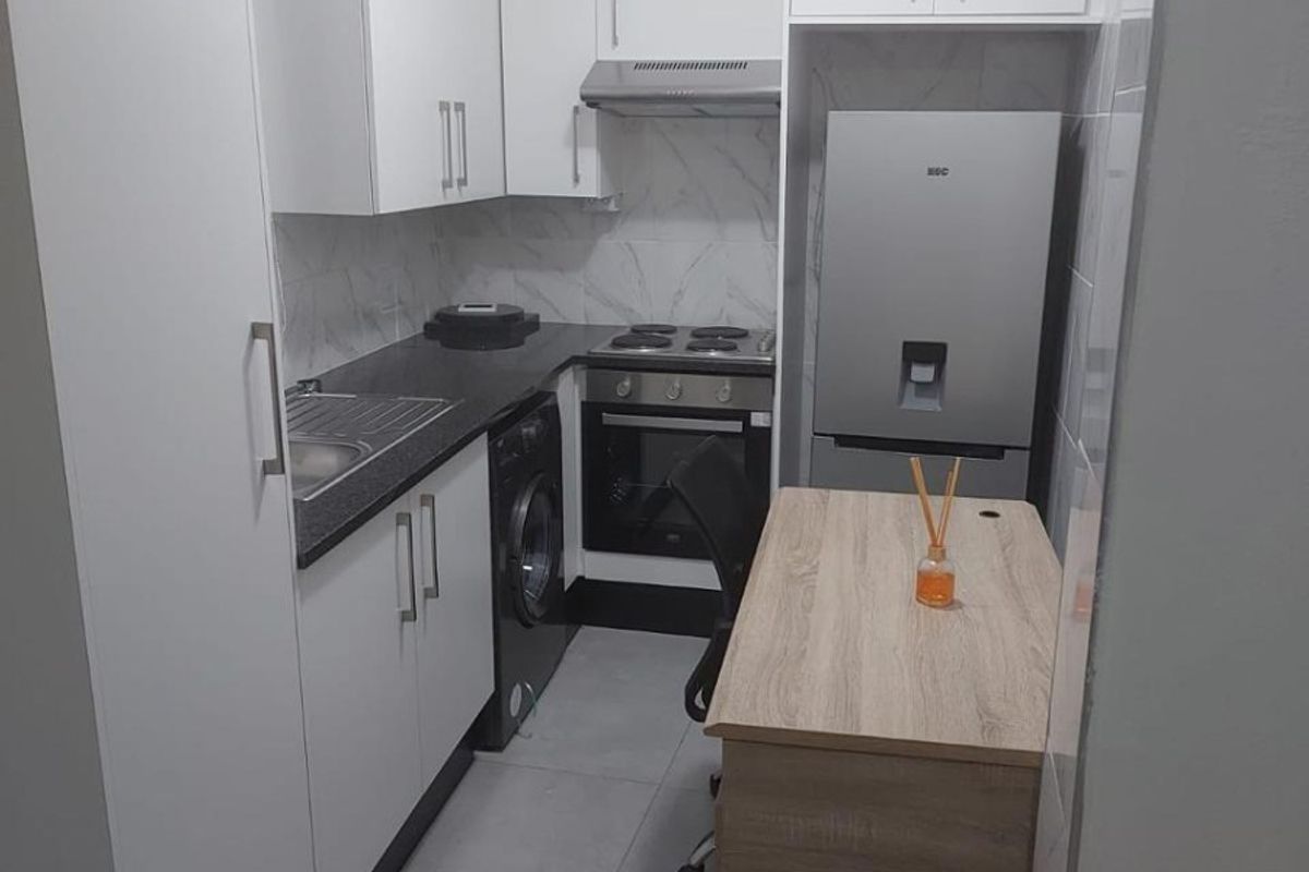 Compact modern kitchen featuring white cabinetry, dark countertops, built-in oven with extractor fan, and tiled finishes.