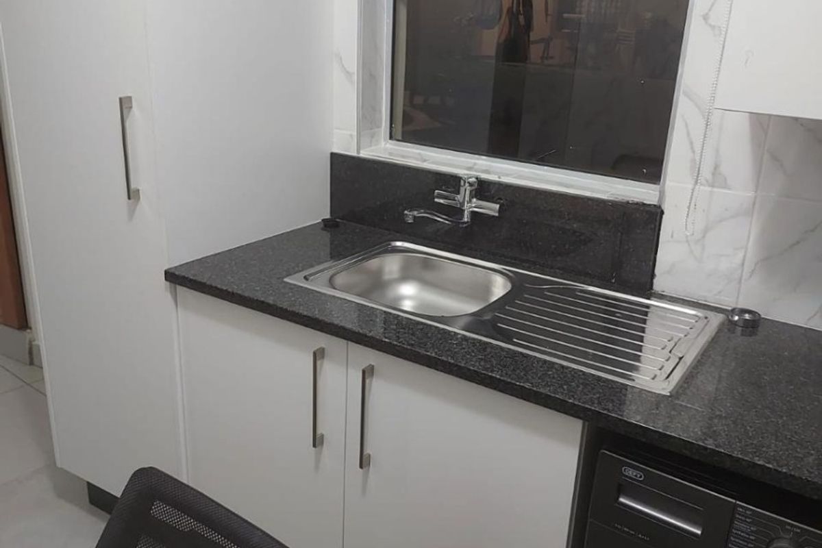 A functional laundry area featuring modern white cabinetry, a dark granite countertop, and a stainless steel sink with a window view.