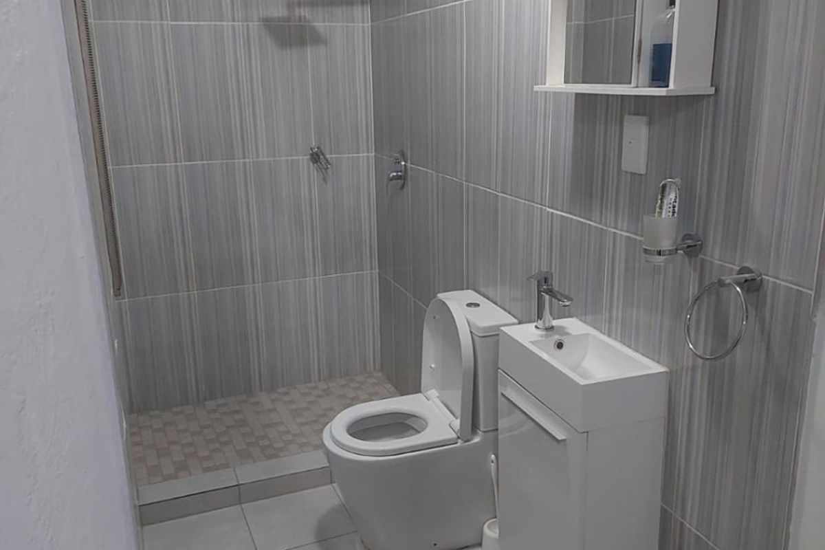 A modern, compact bathroom featuring a walk-in shower, wall-mounted vanity, and neutral grey tiled finishes throughout.