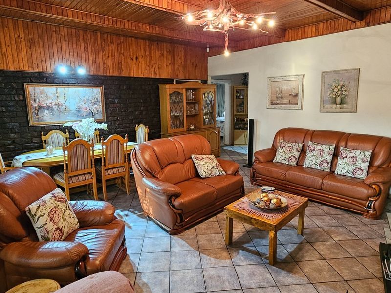 Spacious open-plan living and dining area featuring exposed timber ceilings, brick feature wall, and tiled flooring.