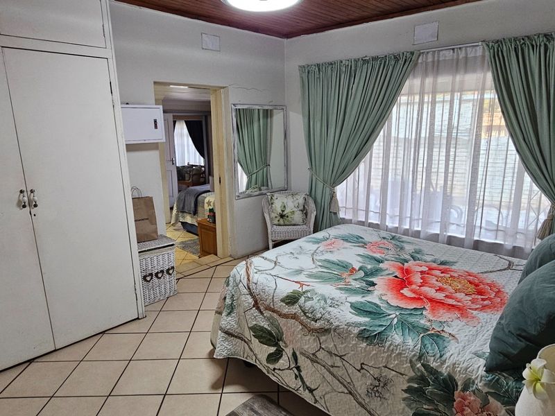 A bedroom featuring built-in cupboards, tiled flooring, and a timber ceiling, with a view into an adjacent room.