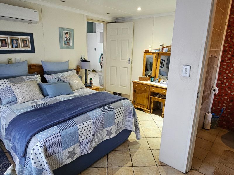 A bedroom featuring tiled flooring, a split-system air conditioner, and an open-plan en-suite bathroom with a distinctive pebble-dash feature wall.