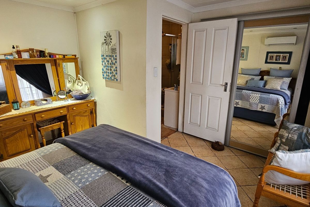 A bedroom featuring tiled flooring, built-in cupboards with mirrored sliding doors, and an integrated air conditioning unit, with direct access to an en-suite bathroom.