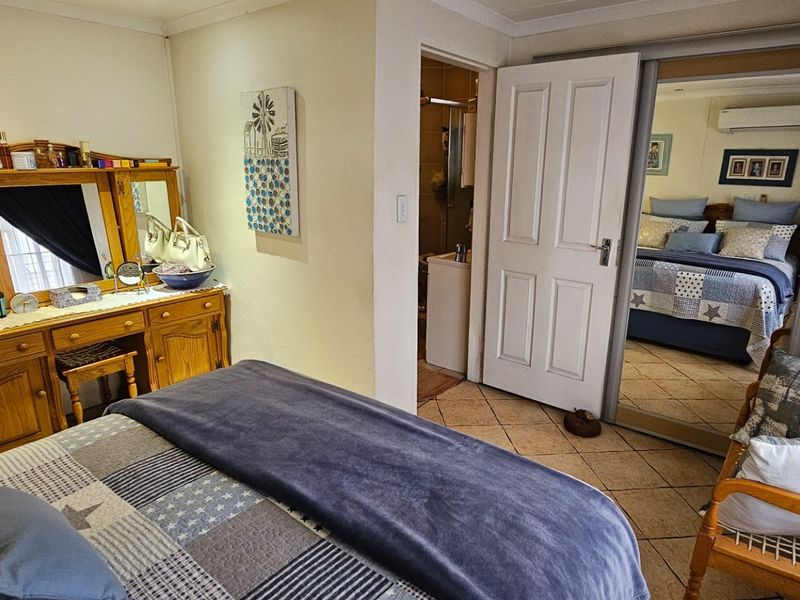 A bedroom featuring tiled flooring, built-in cupboards with mirrored sliding doors, and an integrated air conditioning unit, with direct access to an en-suite bathroom.