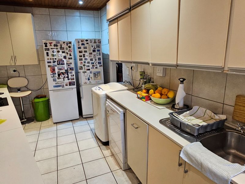A functional kitchen featuring built-in cabinetry, tiled backsplash, stainless steel sink, and timber ceiling, offering a practical layout for daily use.