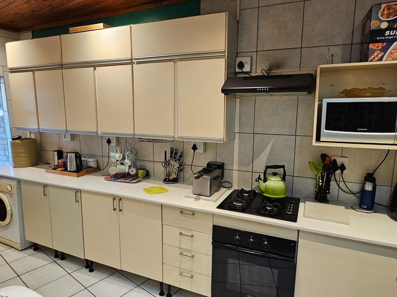 A functional kitchen featuring built-in cabinetry, a gas hob, an electric oven, and an integrated extractor fan with tiled finishes throughout.
