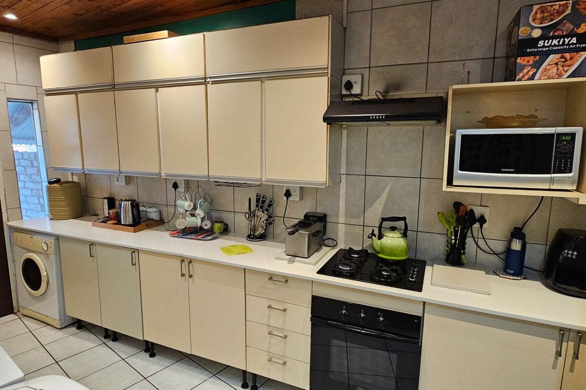 A functional kitchen featuring built-in cabinetry, a gas hob, an electric oven, and an integrated extractor fan with tiled finishes throughout.