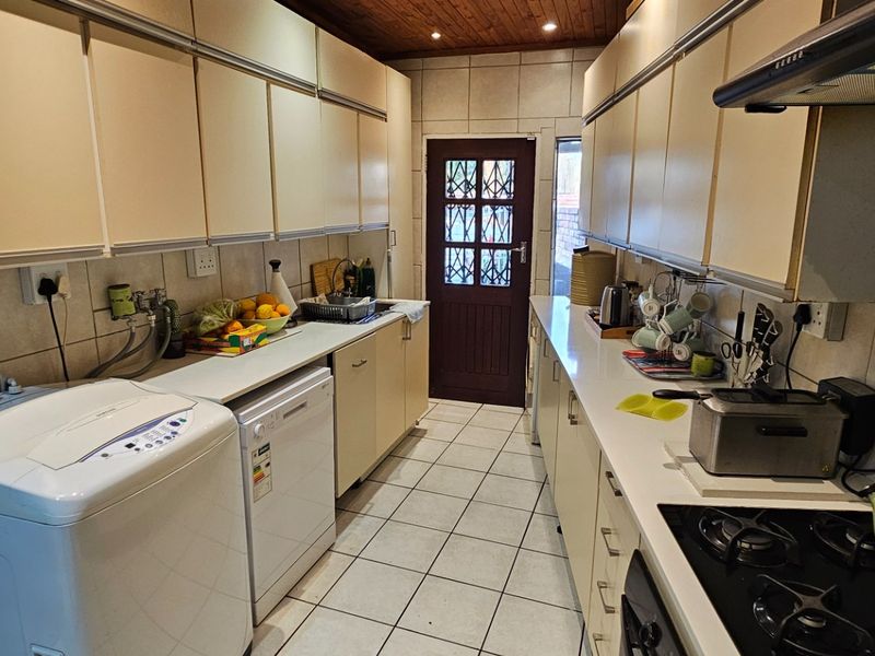 A functional galley-style kitchen featuring tiled flooring, ample built-in cabinetry, a gas hob with extractor fan, and a timber-paneled ceiling.