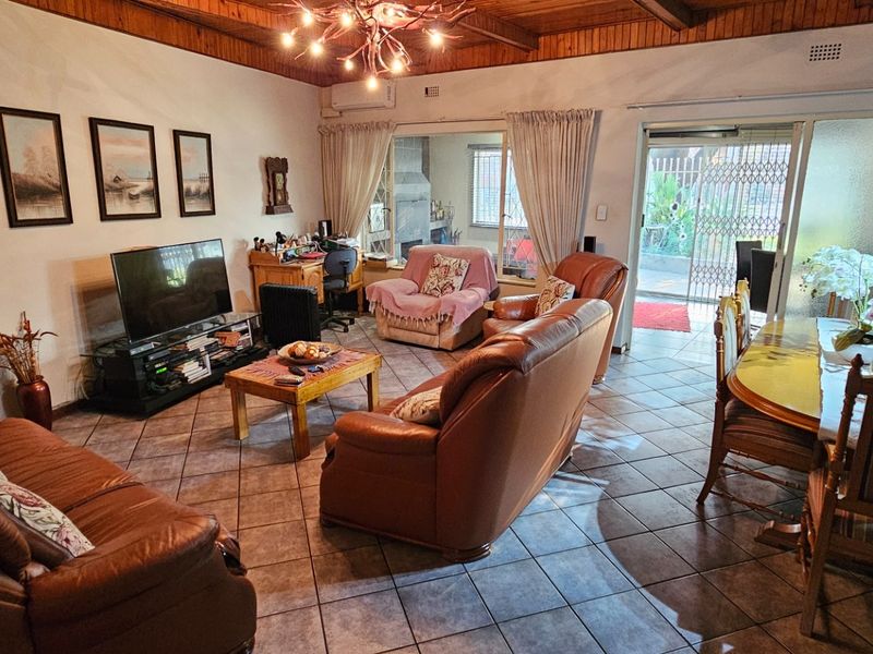 Spacious open-plan living and dining area featuring tiled floors, exposed timber beam ceilings, and direct access to an outdoor patio through sliding glass doors.
