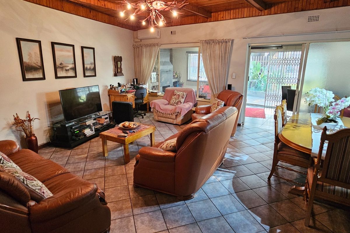 Spacious open-plan living and dining area featuring tiled floors, exposed timber beam ceilings, and direct access to an outdoor patio through sliding glass doors.