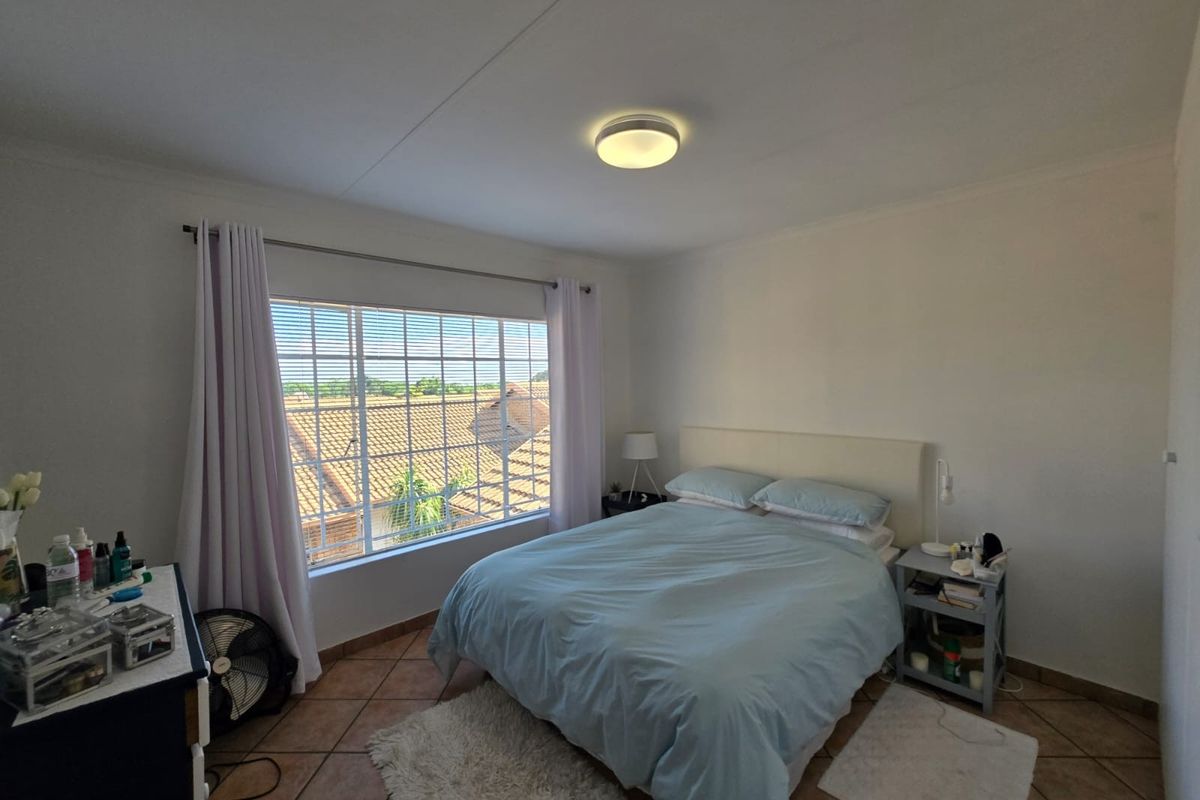 A well-lit bedroom featuring tiled flooring and a large window providing natural light and an elevated view of the surrounding neighborhood.