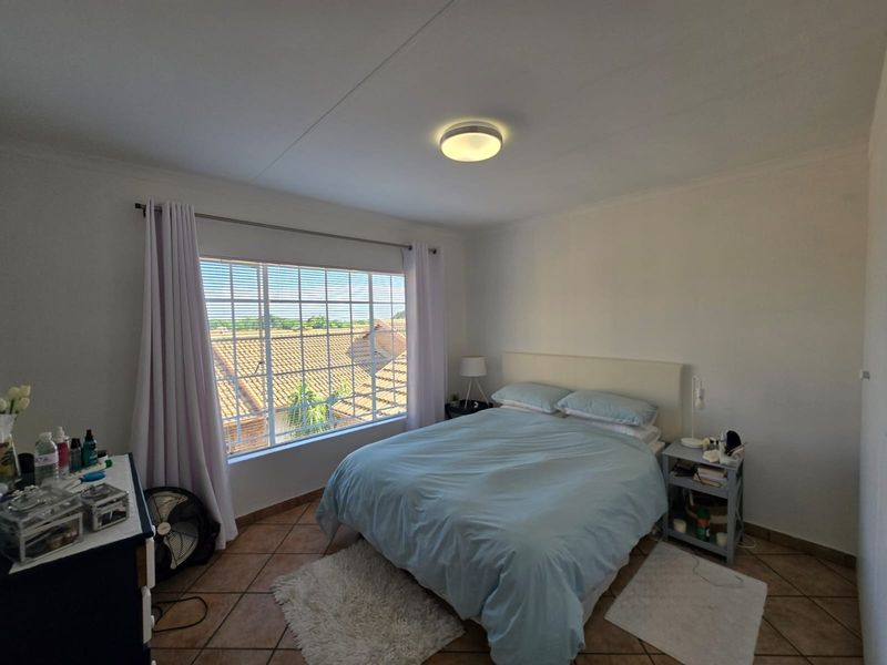A well-lit bedroom featuring tiled flooring and a large window providing natural light and an elevated view of the surrounding neighborhood.