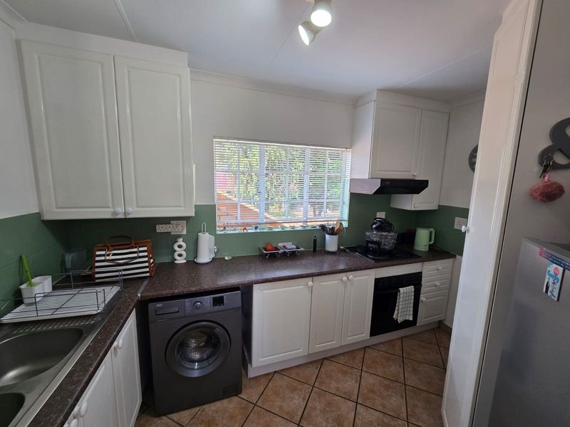 A functional kitchen featuring white cabinetry, dark laminate countertops, a built-in oven with extractor fan, and tiled flooring.