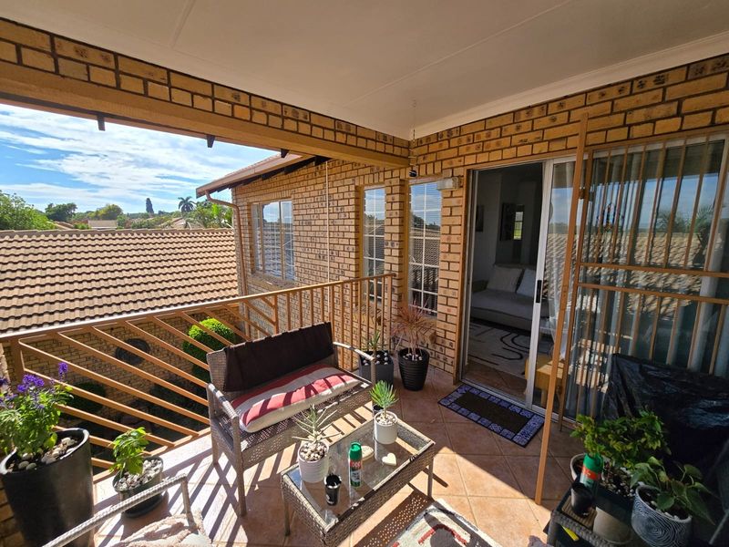 A covered balcony featuring exposed brick walls, tiled flooring, and a metal balustrade, offering an outdoor space accessible through a sliding glass door.