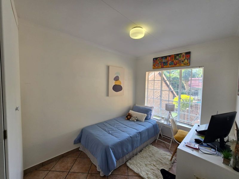 A functional bedroom featuring tiled flooring, a window with fitted blinds, and a central ceiling light fixture.