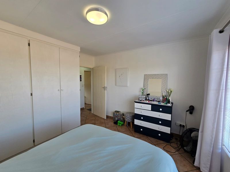A functional bedroom featuring built-in cupboards, tiled flooring, and neutral wall finishes, offering a clean and practical living space.
