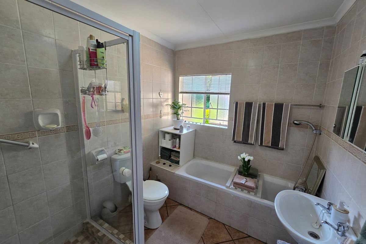 A functional bathroom featuring a separate shower enclosure, bathtub, pedestal basin, and toilet with neutral wall and floor tiling.