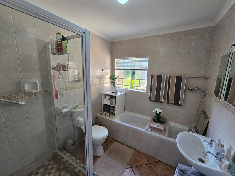 A functional bathroom featuring a separate shower enclosure, bathtub, pedestal basin, and toilet with neutral wall and floor tiling.