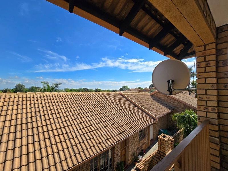 An elevated balcony view overlooking the tiled roofs of the townhouse complex, featuring a mounted satellite dish and brick exterior finishes.