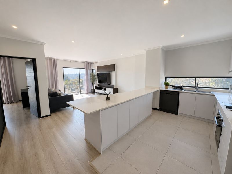 Modern open-plan kitchen and living area featuring a central island, sleek cabinetry, integrated appliances, and seamless transition to a balcony with scenic views.