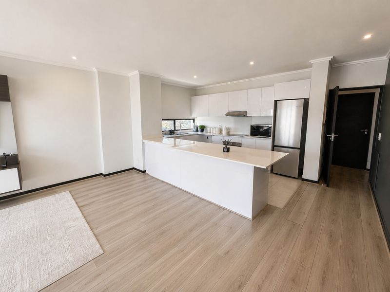 Modern open-plan living area featuring a sleek kitchen with glossy cabinetry, quartz countertops, a central island, and light wood-look laminate flooring.
