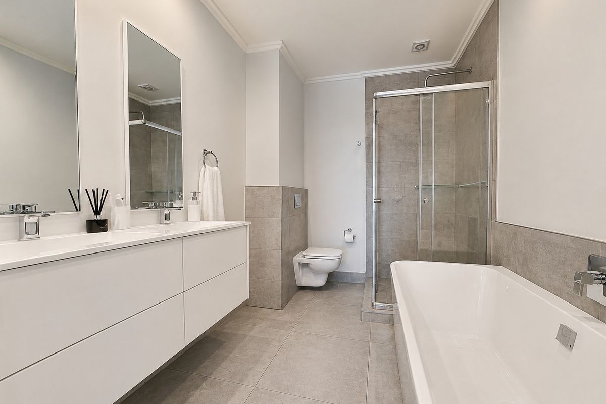 Modern bathroom featuring a double vanity, wall-mounted toilet, glass shower enclosure, and a sleek freestanding bathtub with neutral tiled finishes.