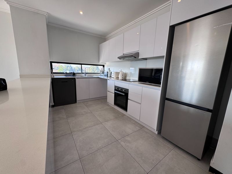 Modern kitchen featuring sleek white gloss cabinetry, stone countertops, integrated appliances, and large format floor tiles in a clean, contemporary layout.