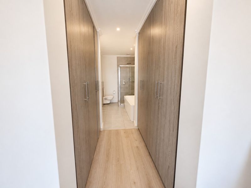 A clean hallway featuring extensive built-in wooden cabinetry leading directly into a modern bathroom with a shower and bathtub.