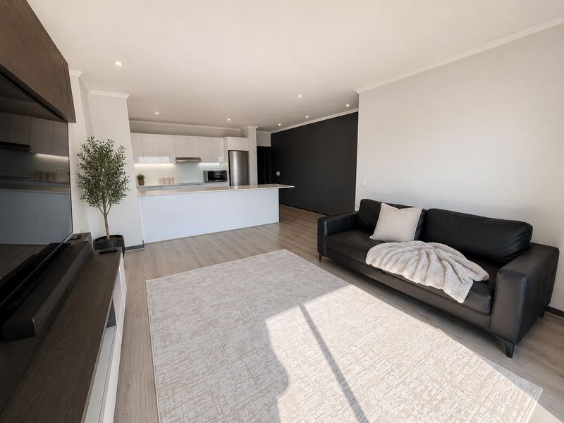 Modern open-plan living area featuring a sleek kitchen with white cabinetry, a central island, and light-toned laminate flooring throughout the space.