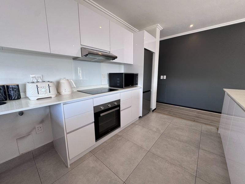 Modern kitchen featuring white gloss cabinetry, stone countertops, built-in oven, electric hob, and integrated appliances with sleek tiled flooring.