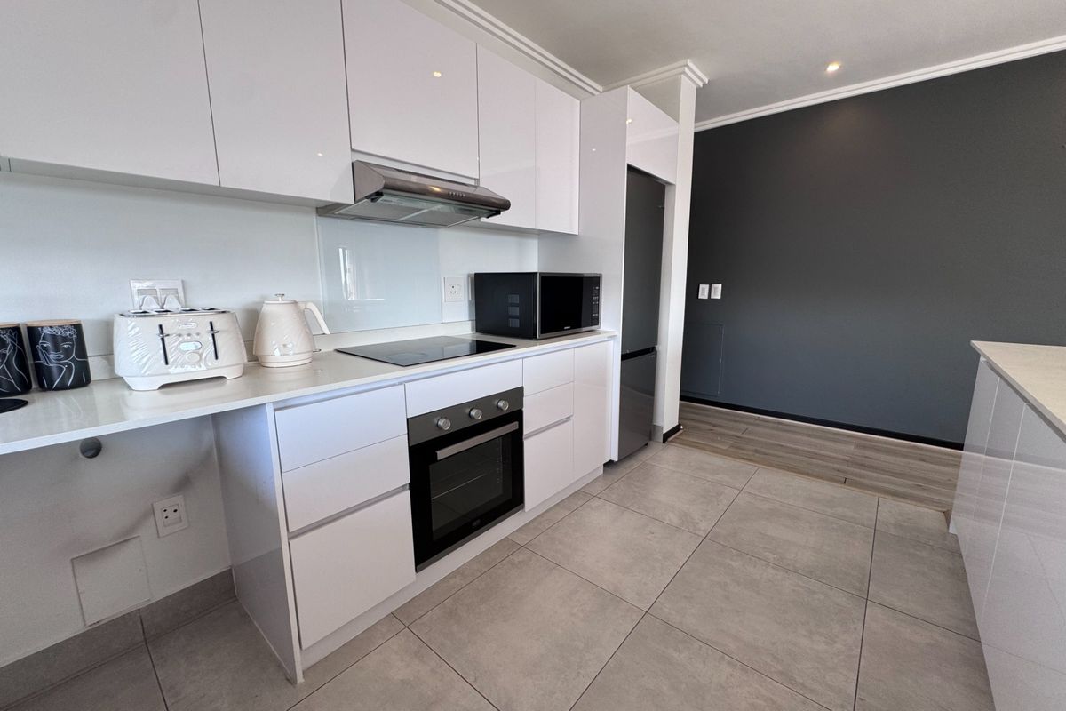 Modern kitchen featuring white gloss cabinetry, stone countertops, built-in oven, electric hob, and integrated appliances with sleek tiled flooring.