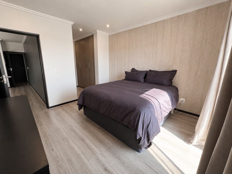 A well-maintained bedroom featuring light laminate flooring, textured feature wallpaper, and built-in cupboards with a neutral, modern aesthetic.