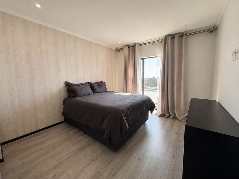 A well-maintained bedroom featuring light-toned laminate flooring, textured feature wallpaper, recessed lighting, and a sliding glass door providing natural light.