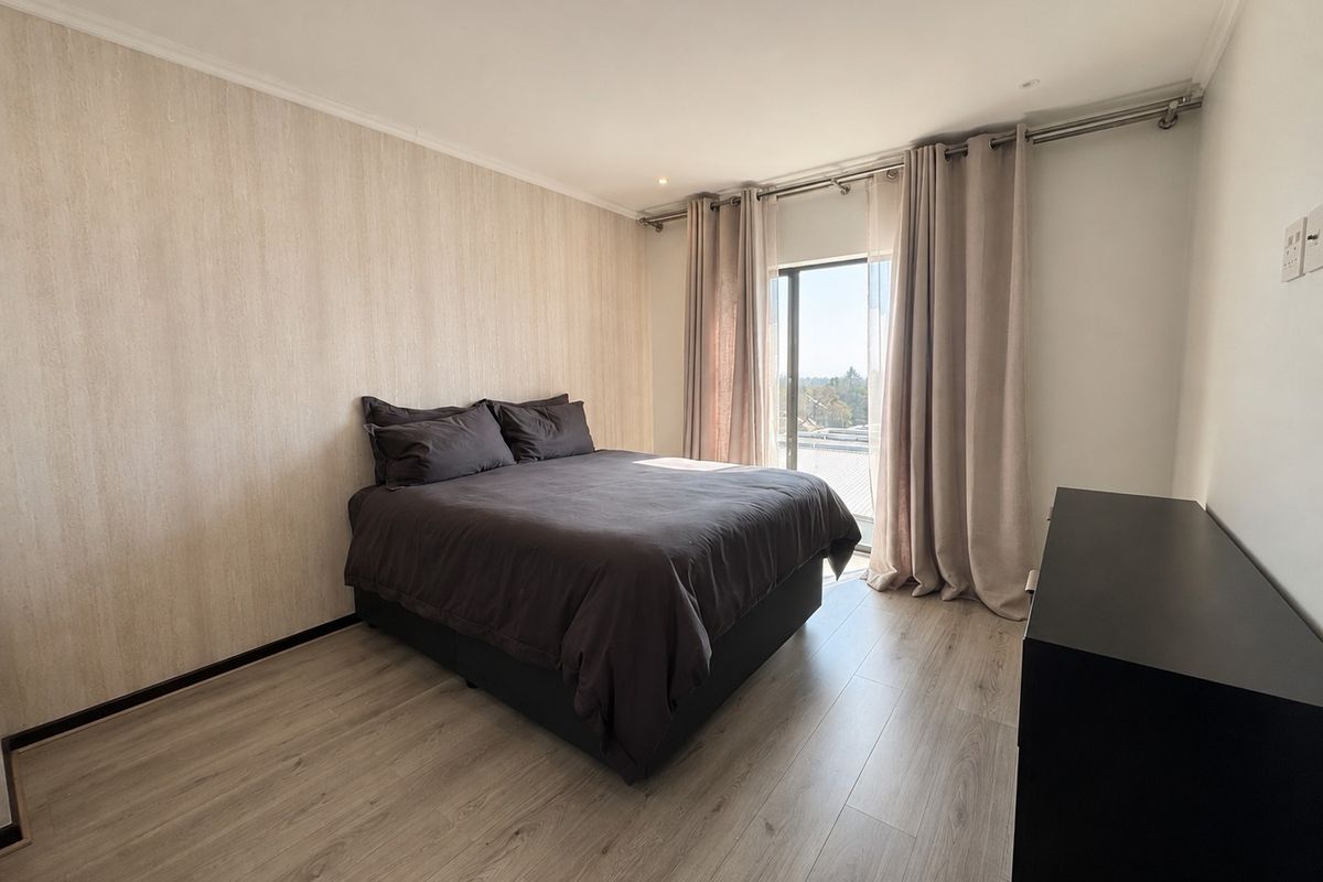 A well-maintained bedroom featuring light-toned laminate flooring, textured feature wallpaper, recessed lighting, and a sliding glass door providing natural light.