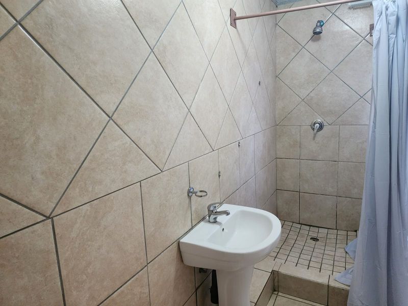 A functional bathroom featuring a pedestal washbasin and a shower area with tiled walls and flooring, requiring some maintenance and cosmetic updates.