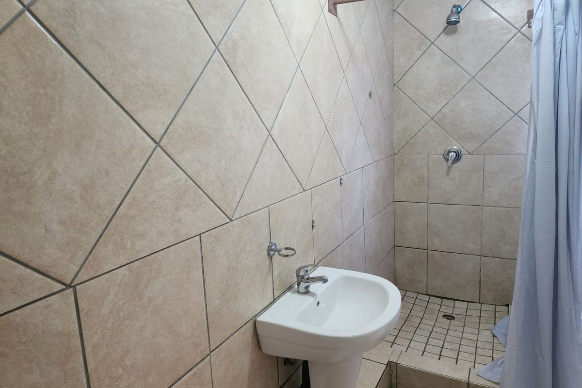 A functional bathroom featuring a pedestal washbasin and a shower area with tiled walls and flooring, requiring some maintenance and cosmetic updates.