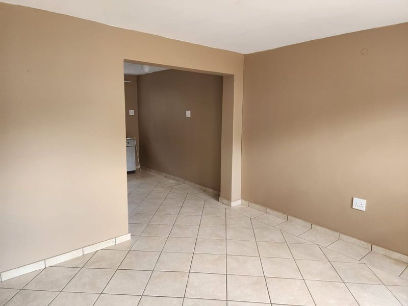An empty open-plan living area featuring neutral-toned walls and ceramic floor tiles, providing a blank canvas for interior design.