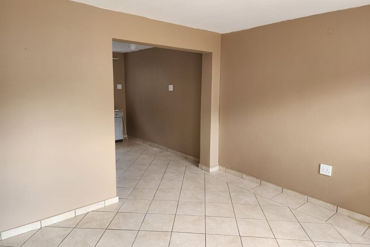 An empty open-plan living area featuring neutral-toned walls and ceramic floor tiles, providing a blank canvas for interior design.