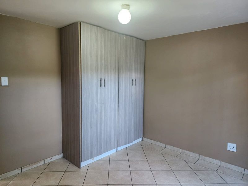 An empty bedroom featuring neutral wall paint, tiled flooring, and a modern built-in wardrobe with wood-grain finish.