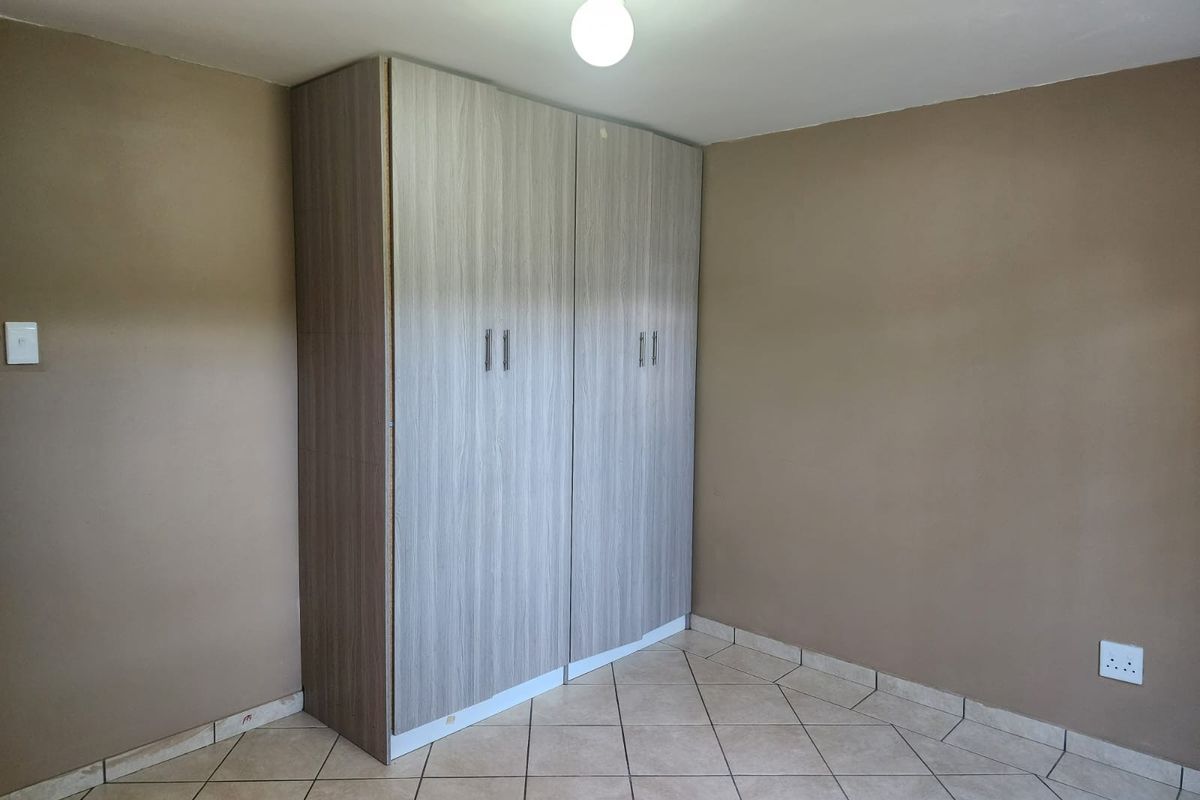 An empty bedroom featuring neutral wall paint, tiled flooring, and a modern built-in wardrobe with wood-grain finish.