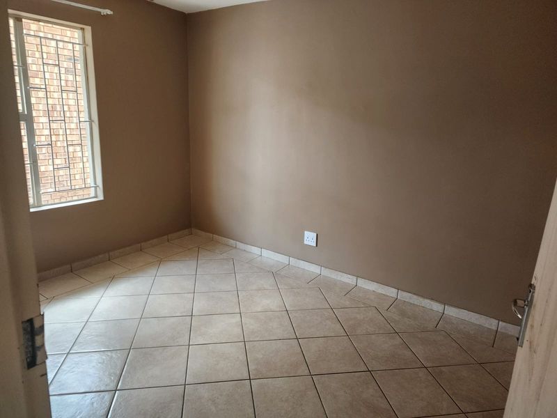 An empty bedroom featuring neutral wall paint, tiled flooring, and a window fitted with security bars.