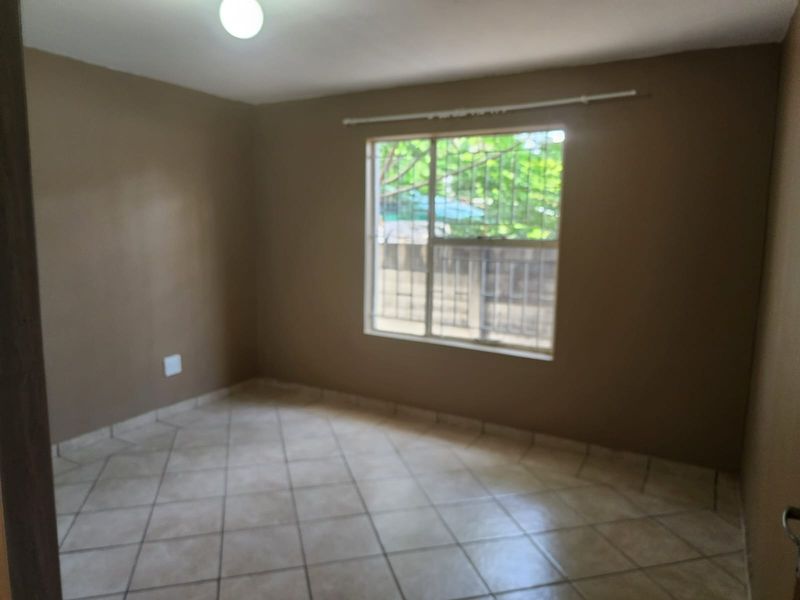 An empty bedroom featuring tiled flooring, a window with security bars, and a curtain rod, providing a blank canvas for personalization.