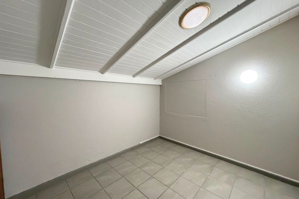An empty bedroom featuring tiled flooring, a raked ceiling with exposed beams, and dual lighting fixtures.