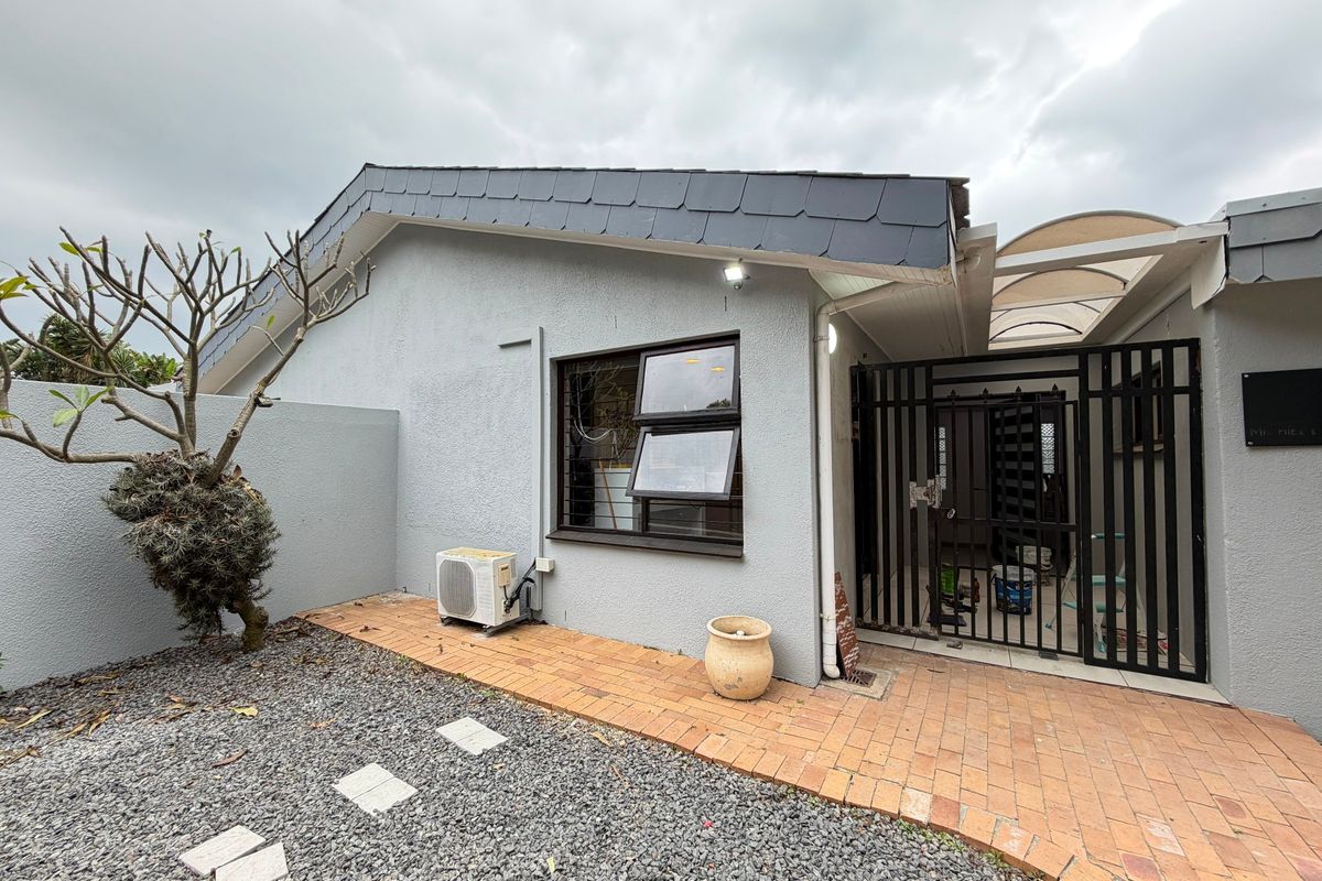 Rear exterior view of the townhouse featuring a paved walkway, security gate, covered patio area, and slate roof tiles.